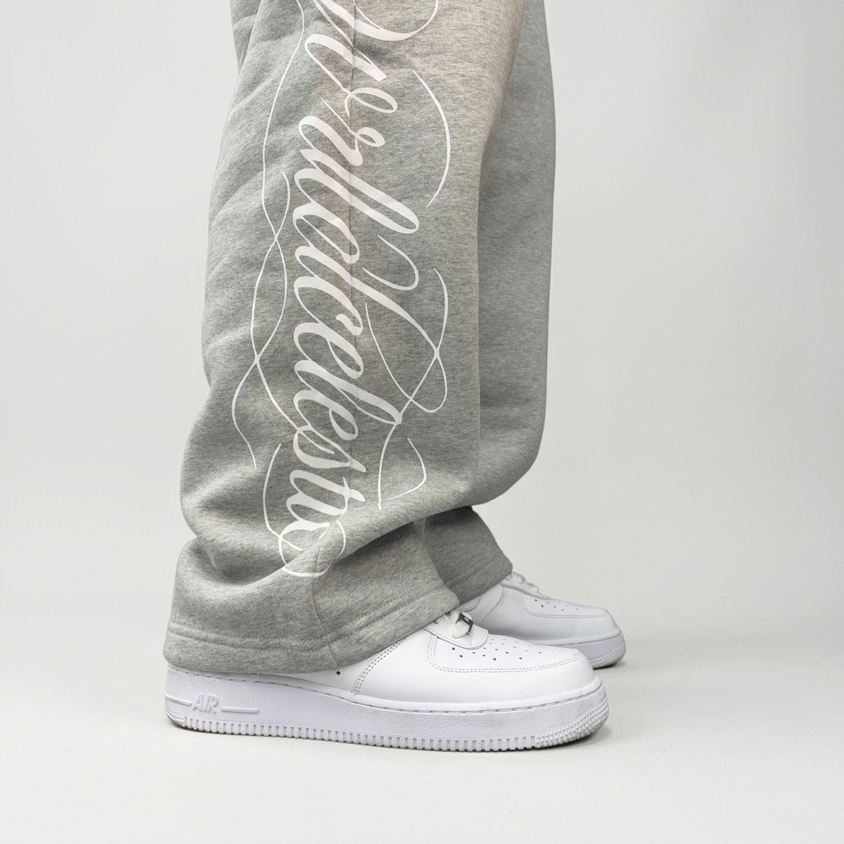 Close-up of the white Wrldcelestic script print on the lower leg of the CELESTIC Grey Script Pants over white sneakers.