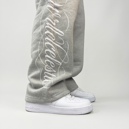 Close-up of the white Wrldcelestic script print on the lower leg of the CELESTIC Grey Script Pants over white sneakers.
