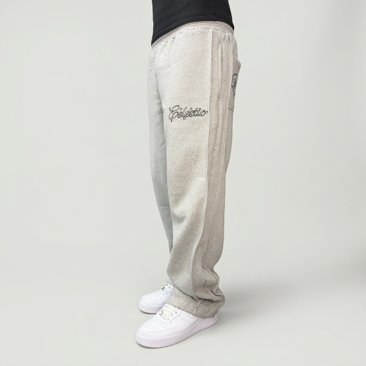 Side view on model of the CELESTIC Grey Outline Pants, relaxed straight-leg fit in heavyweight heather grey cotton fleece over white sneakers.