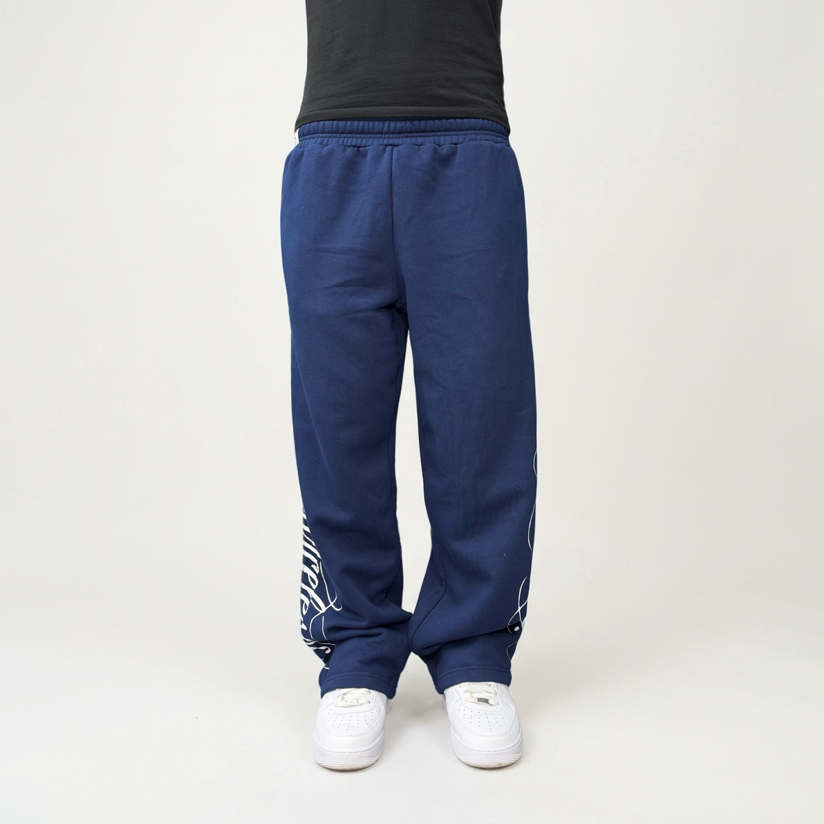 Front view on model of the CELESTIC Navy Blue Script Pants in heavyweight navy cotton fleece, relaxed straight-leg fit over white sneakers.