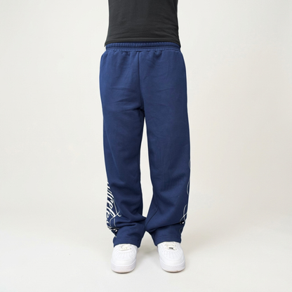 Front view on model of the CELESTIC Navy Blue Script Pants in heavyweight navy cotton fleece, relaxed straight-leg fit over white sneakers.