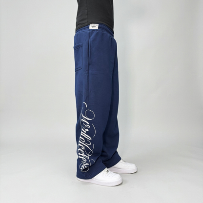 Side view on model of the CELESTIC Navy Blue Script Pants, showing the white Wrldcelestic script print running down the leg.