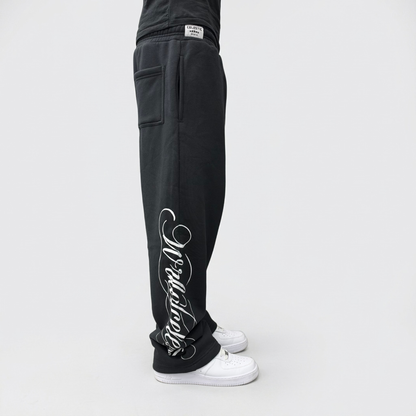Side view on model of the CELESTIC Black Script Pants, showing the white Wrldcelestic script print running down the leg to the hem.