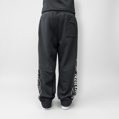Back view on model of the CELESTIC Black Script Pants, showing the white script print on both legs and the relaxed straight-leg fit.