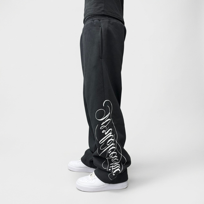 Angled side view on model of the CELESTIC Black Script Pants with white Wrldcelestic script print, styled with white sneakers.